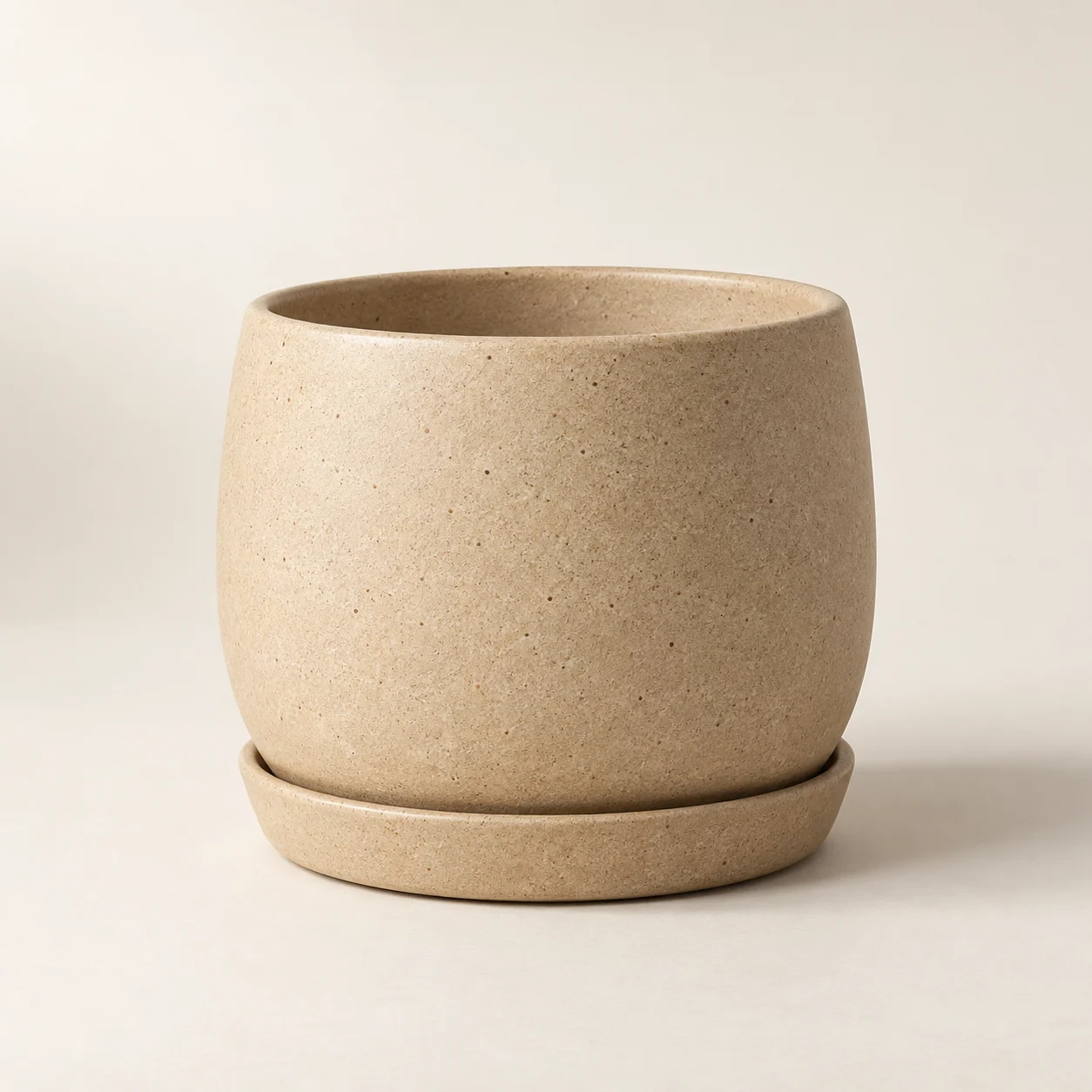 Sand-coloured ceramic planter and saucer against a warm ivory background